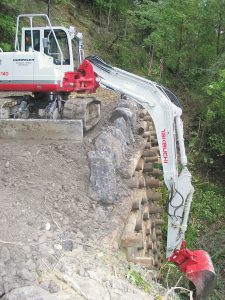 Excavadora compacta Humpeler con brazo hidráulico para trabajos de construcción en terrenos inclinados, equipada con cadenas resistentes y cuchara en entornos rurales y urbanos, ideal para obras de gran envergadura.