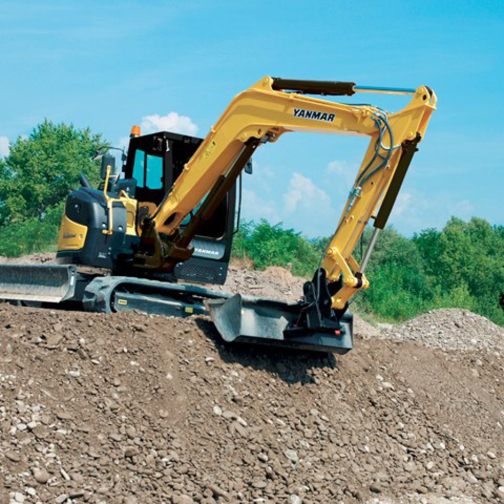 Excavadora amarilla Yanmar en construcción trabajando en terreno con tierra y piedras bajo cielo azul.