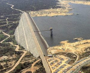 Cauce de presa sobre un embalse con zona de aparcamiento de vehículos y paisajes áridos en el entorno.