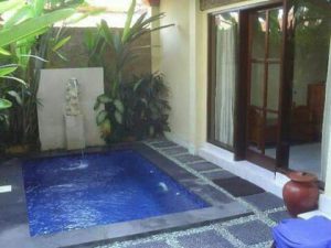 Bañera de hidromasaje exterior en un patio con plantas tropicales y espacio de descanso, ideal para relajarse y disfrutar del lujo en casa.