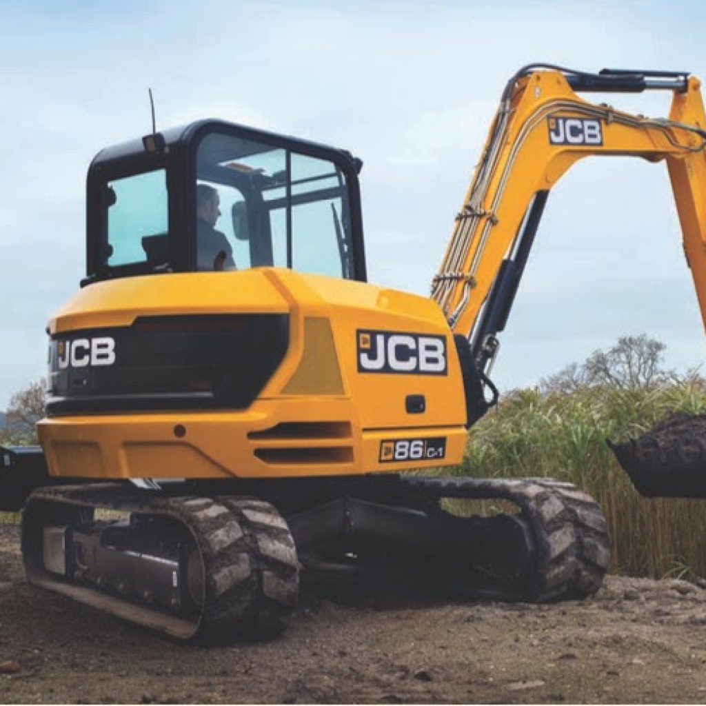 Maquinaria excavadora compacta JCB en obra de construcción, equipada con bandeja y sistema de orugas para trabajos en terrenos difíciles.